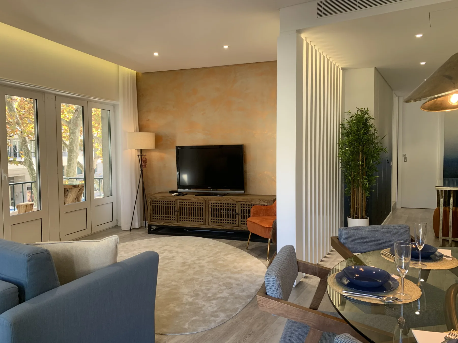 Una sala luminosa con asientos, un televisor y ventanas grandes.