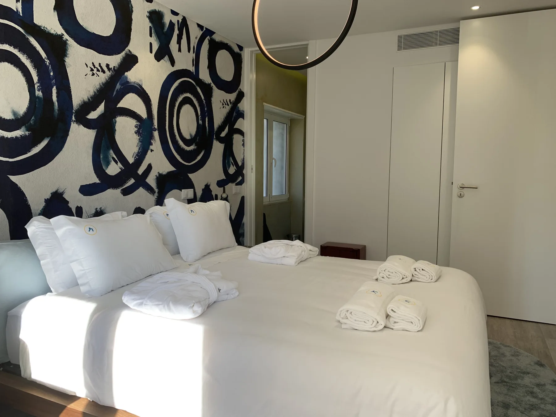 Un dormitorio con una cama grande, ropa de cama blanca y arte abstracto llamativo en la pared.