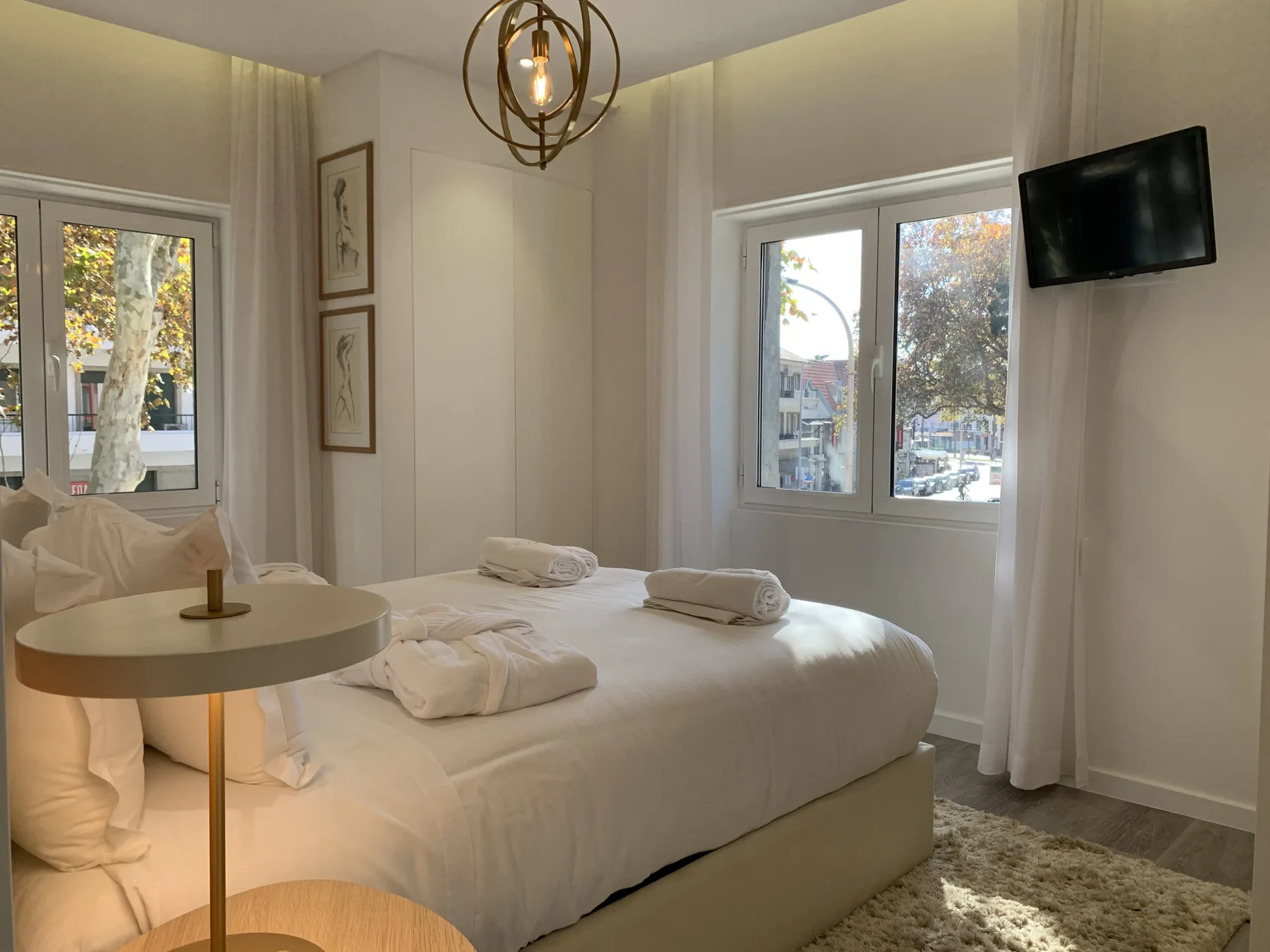Un dormitorio con una cama bien hecha, una mesa auxiliar y ventanas.