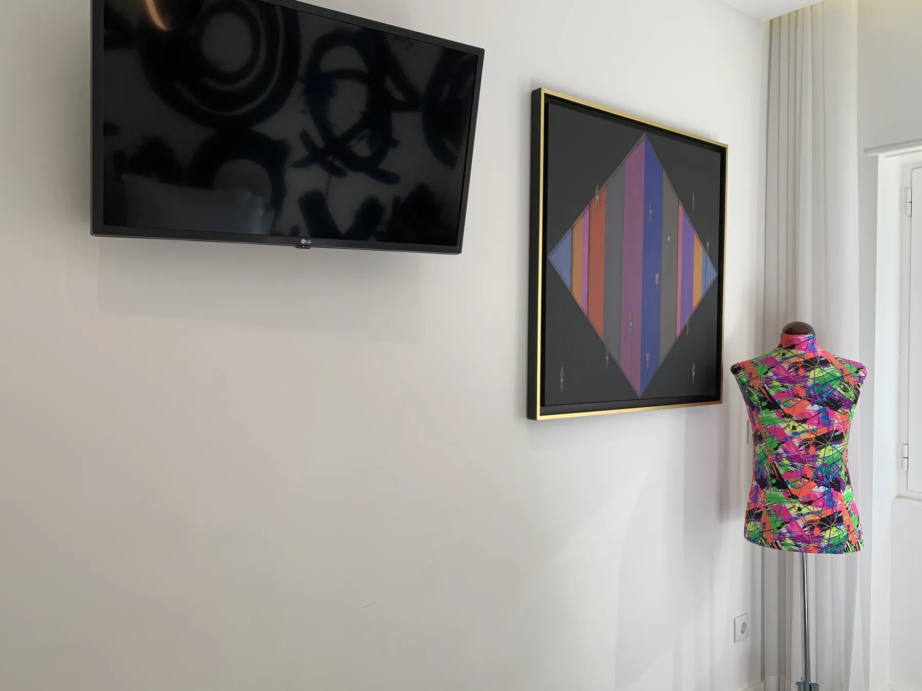 Una pared interior luminosa muestra un televisor, una obra colorida y una prenda estampada.