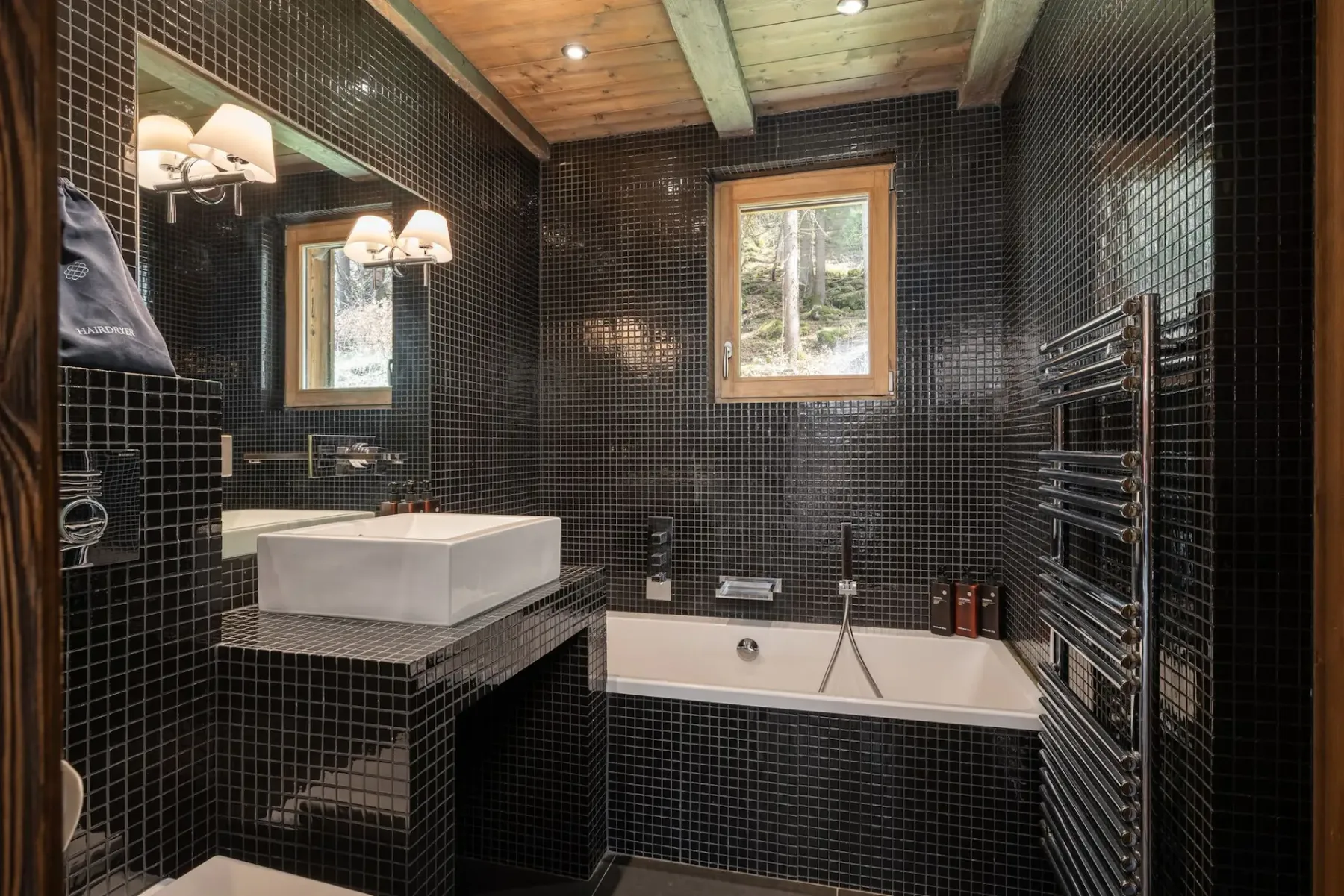 Un baño de azulejos oscuros con bañera y lavabo blanco.
