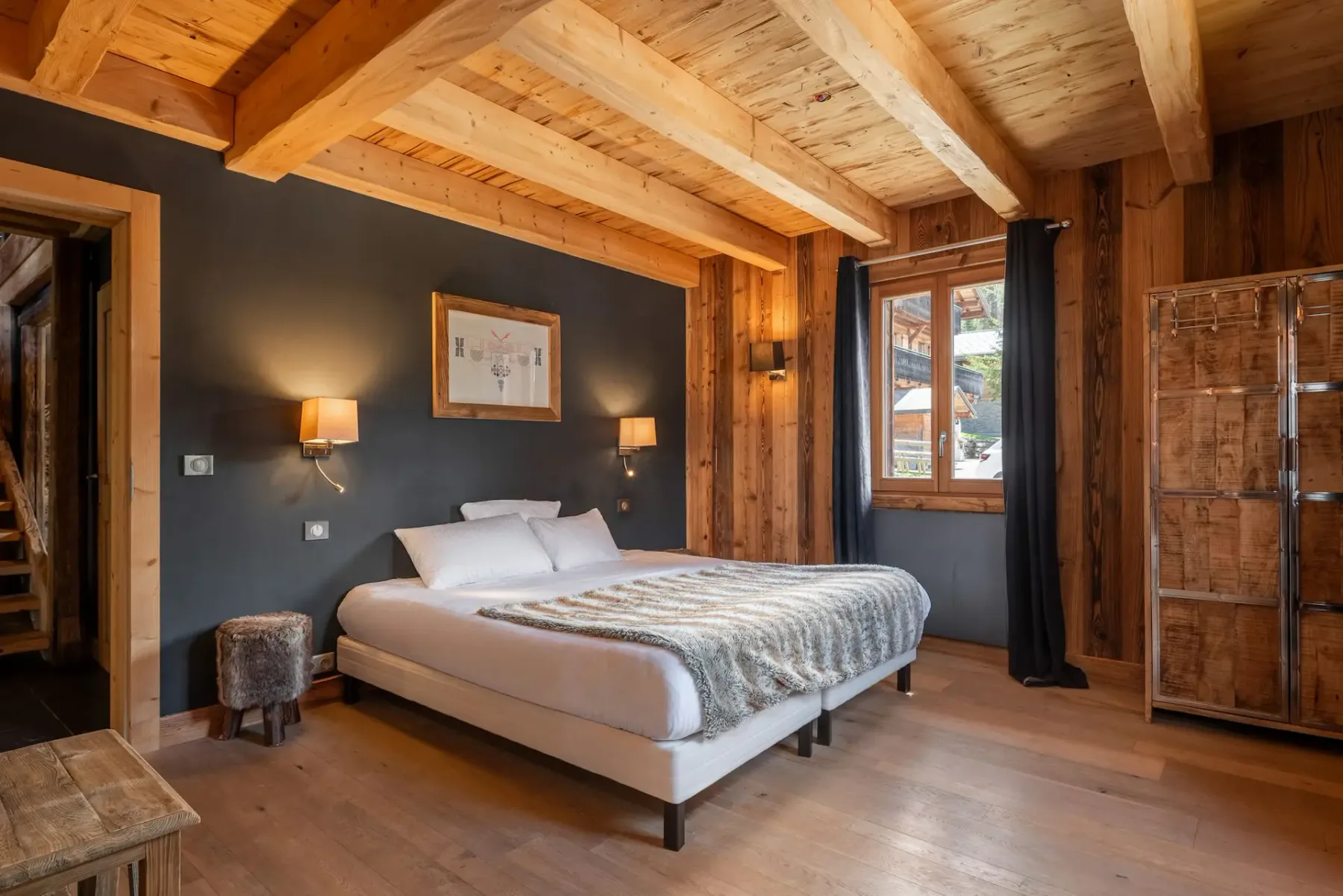 Un dormitorio con una cama, vigas de madera expuestas y una ventana con cortinas oscuras.