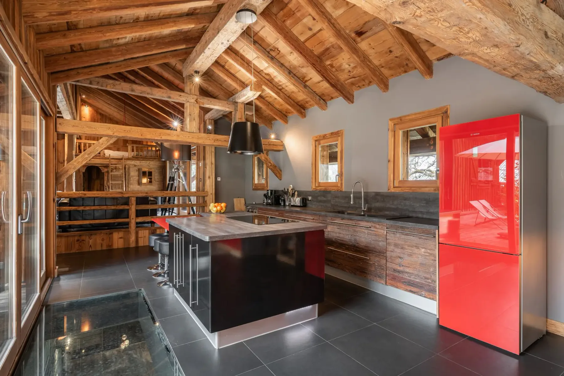 Una cocina rústica con vigas de madera vistas, una isla central y un refrigerador rojo brillante.