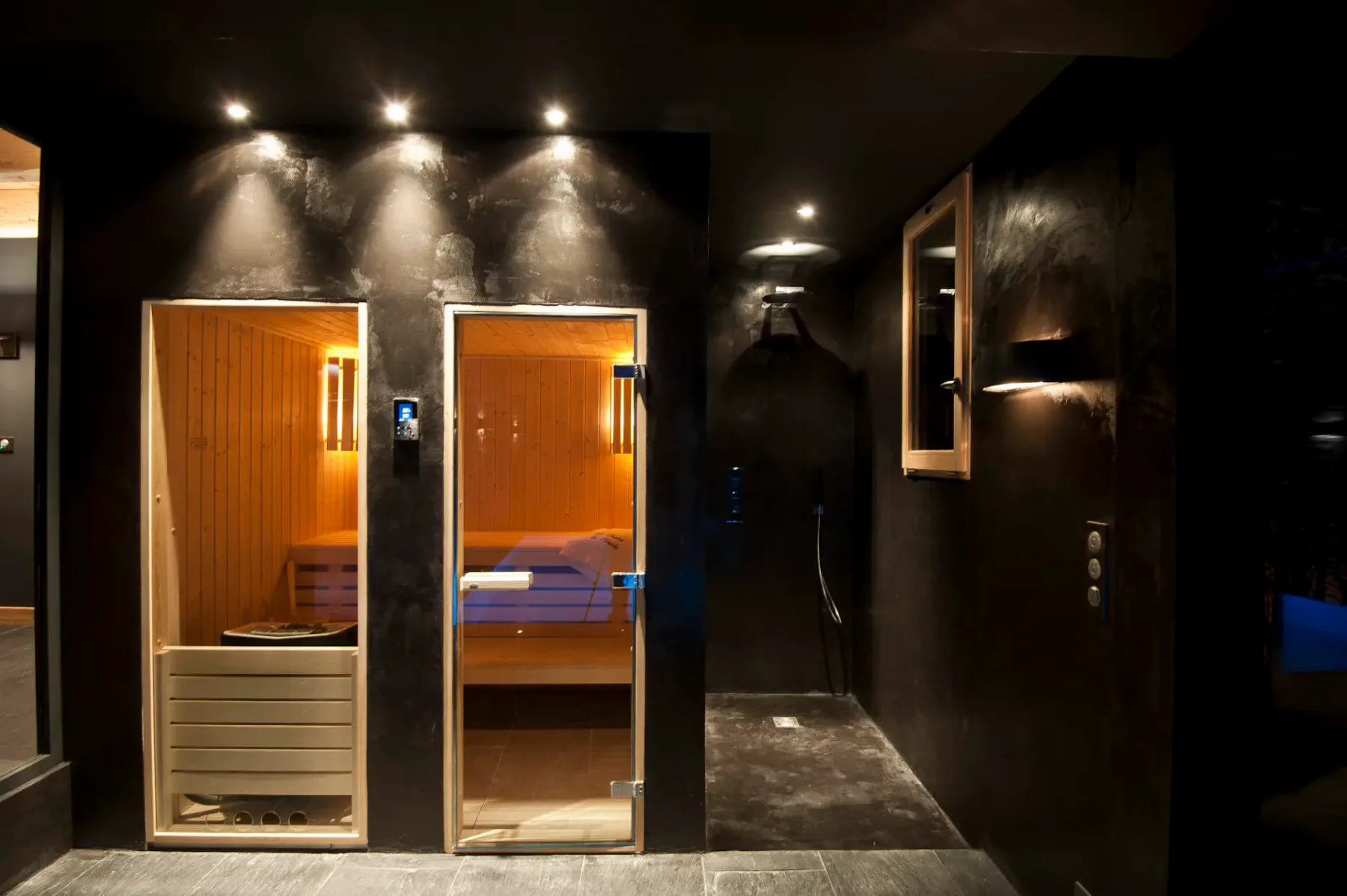 Una sala de spa oscura con dos cabinas de sauna de madera iluminadas y suelo de baldosas.