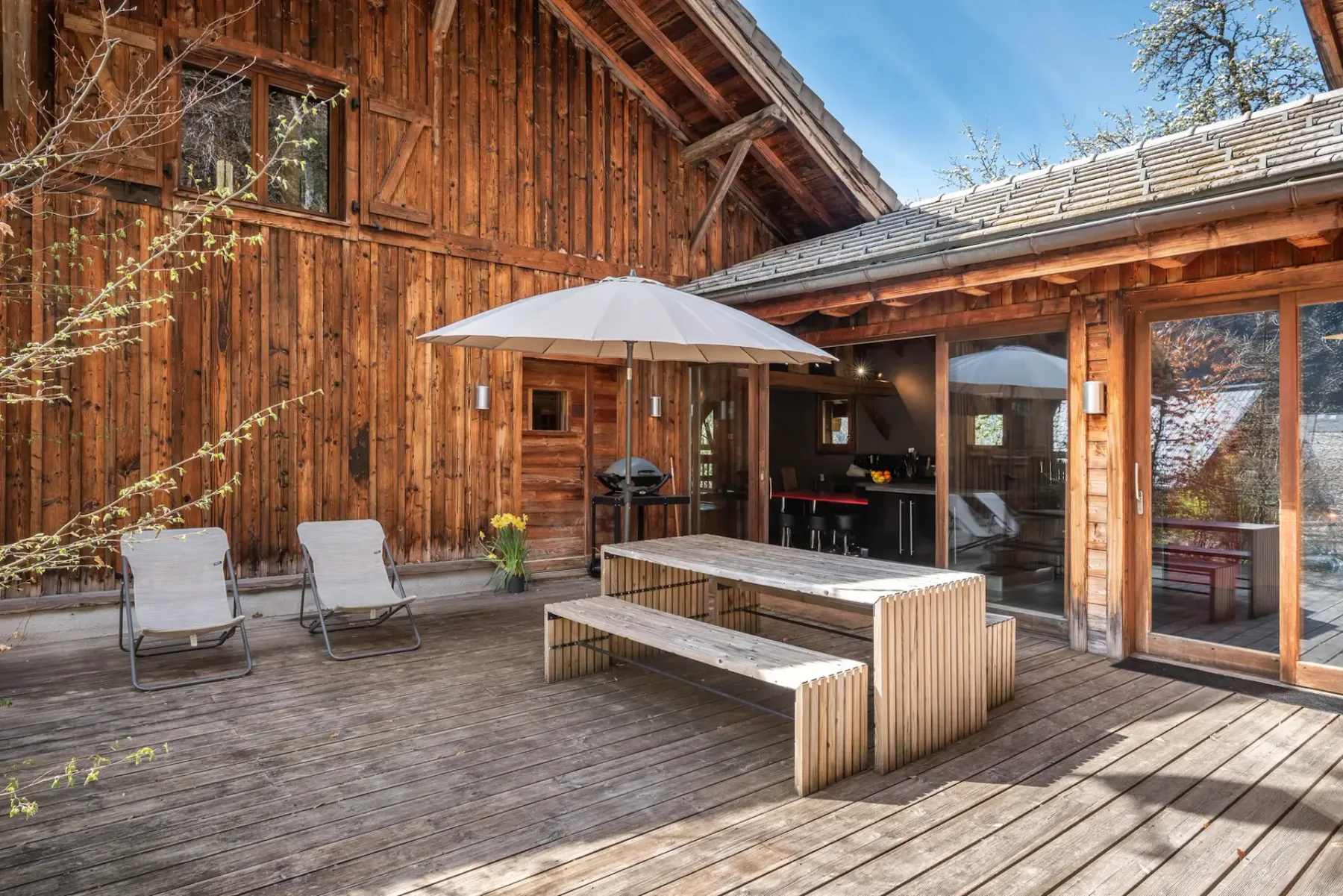 Una terraza exterior de madera con asientos, una mesa y una sombrilla grande.