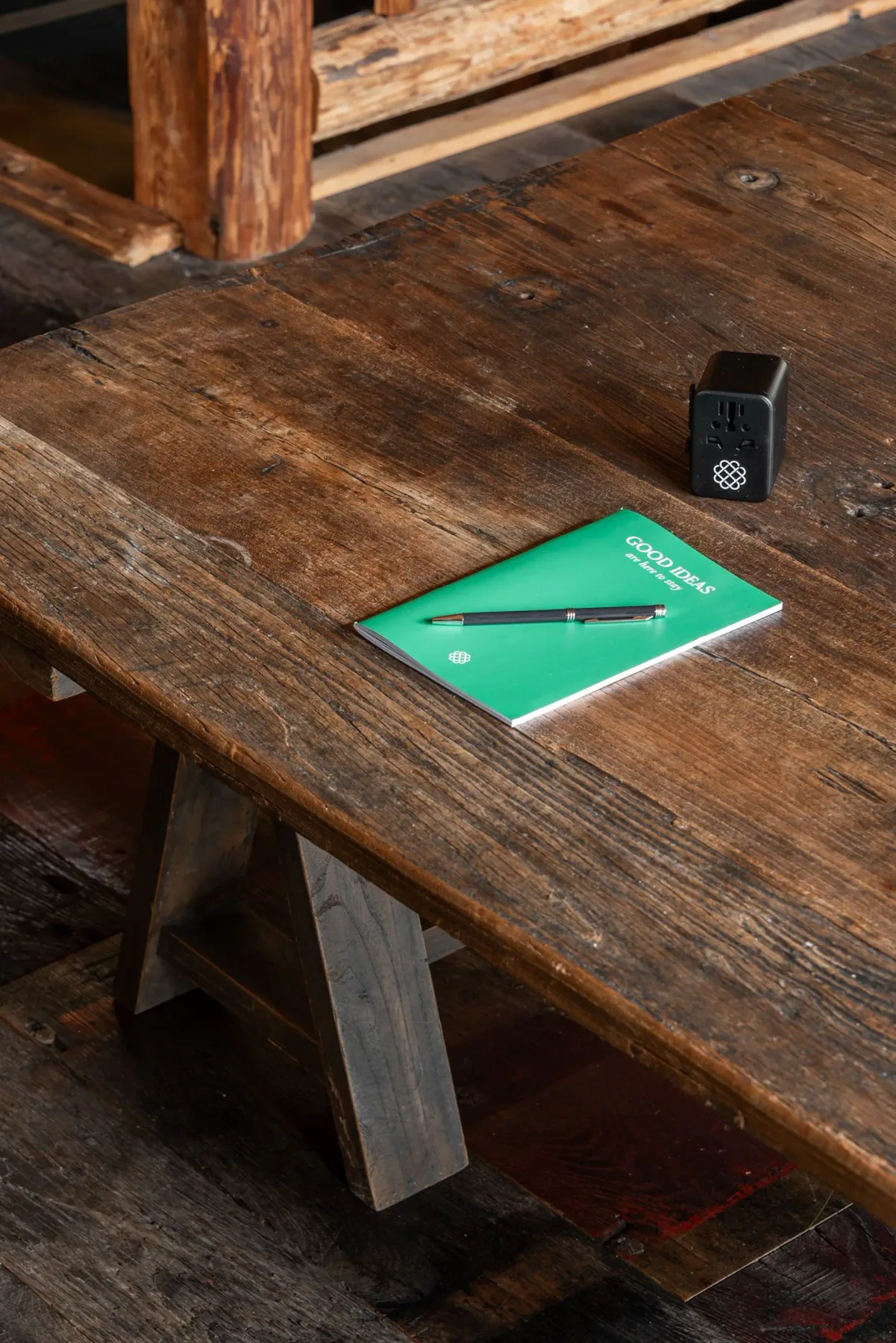 Una mesa de madera desgastada sostiene un folleto verde, un bolígrafo y un pequeño dispositivo negro.