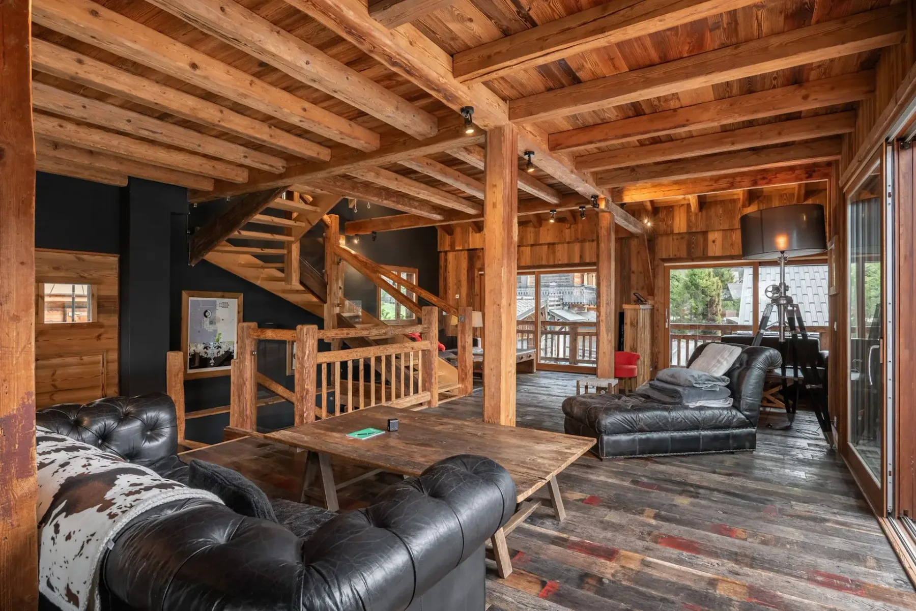 Sala de estar rústica con vigas de madera a la vista, asientos de cuero y grandes ventanales.