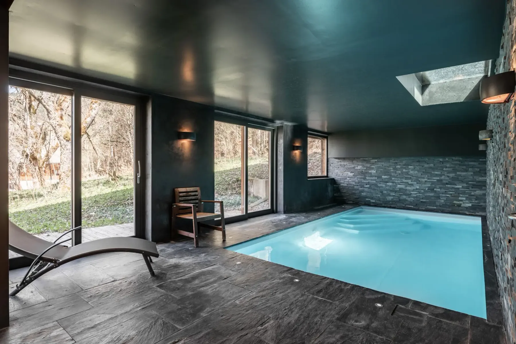 Una piscina interior con grandes ventanas y una zona de asientos junto al agua.
