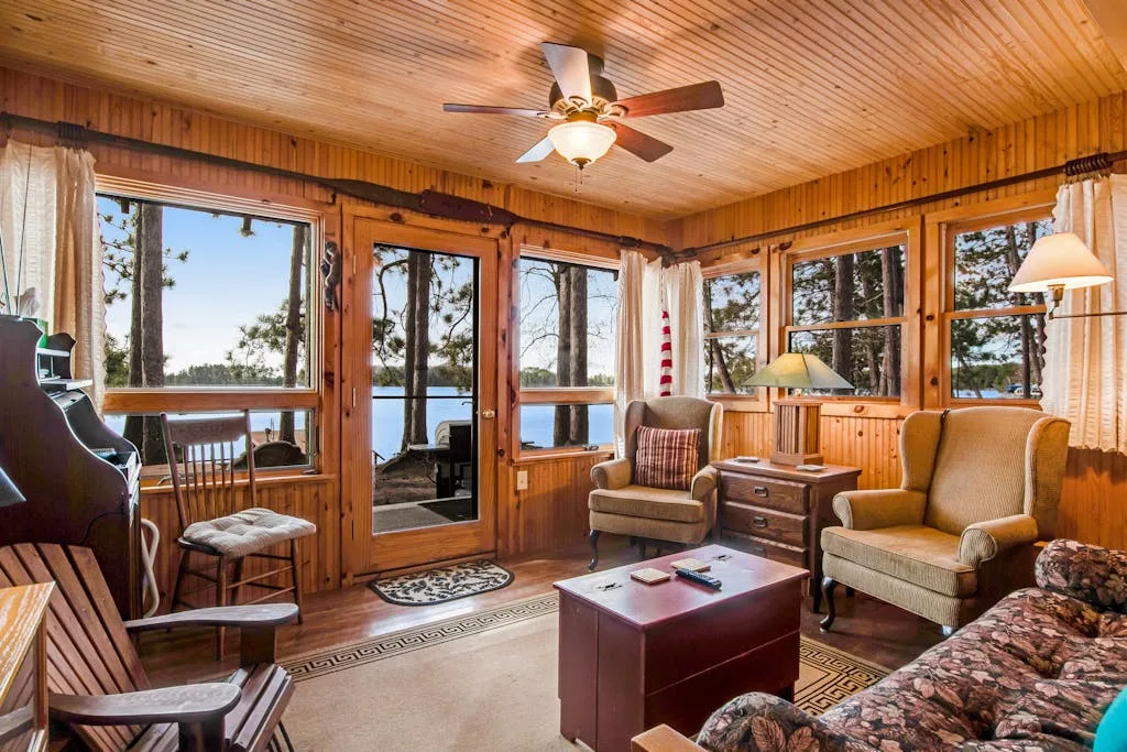 A wood-paneled living room with seating, a coffee table, and large windows overlooking the water.