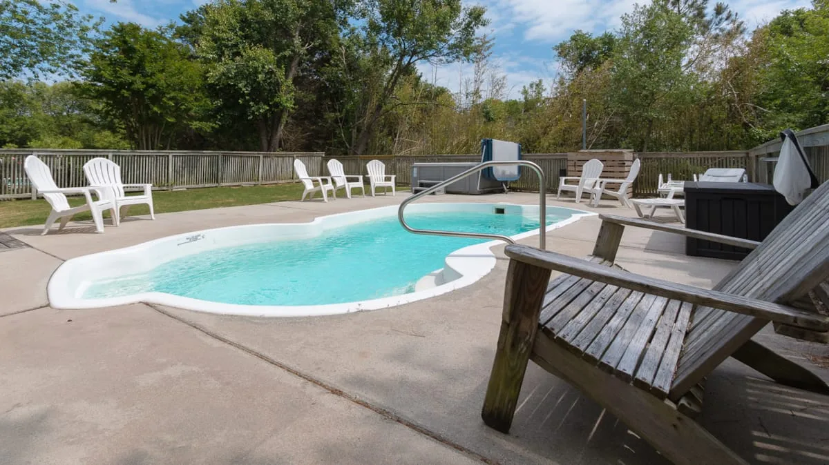 An outdoor swimming pool sits on a paved patio with seating around it.