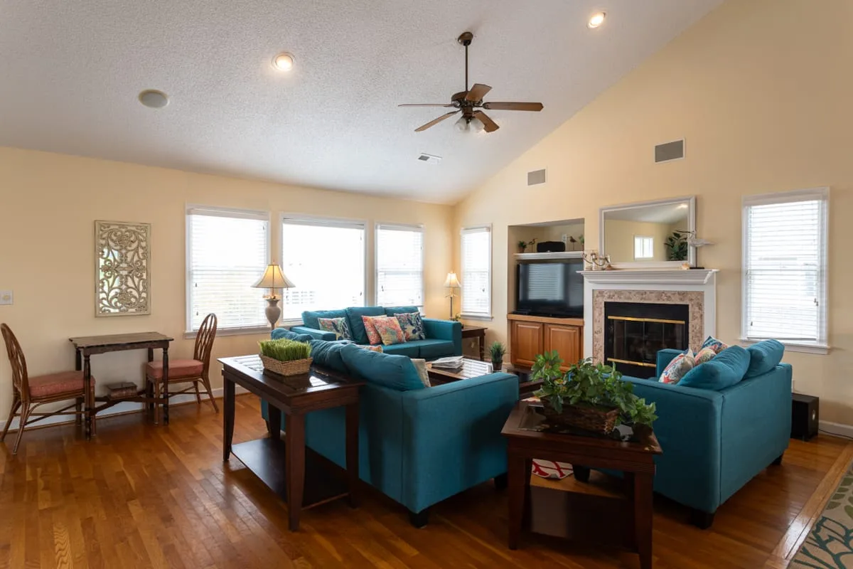 A living room with teal seating arranged around a fireplace and coffee tables.