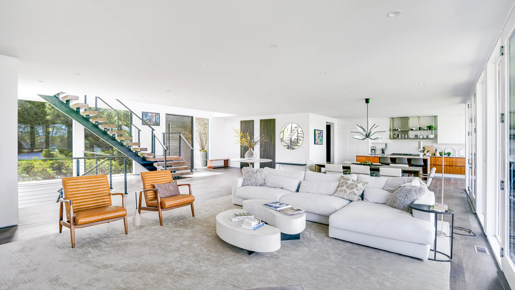 A bright open-plan living room with seating, a dining area, and a staircase.