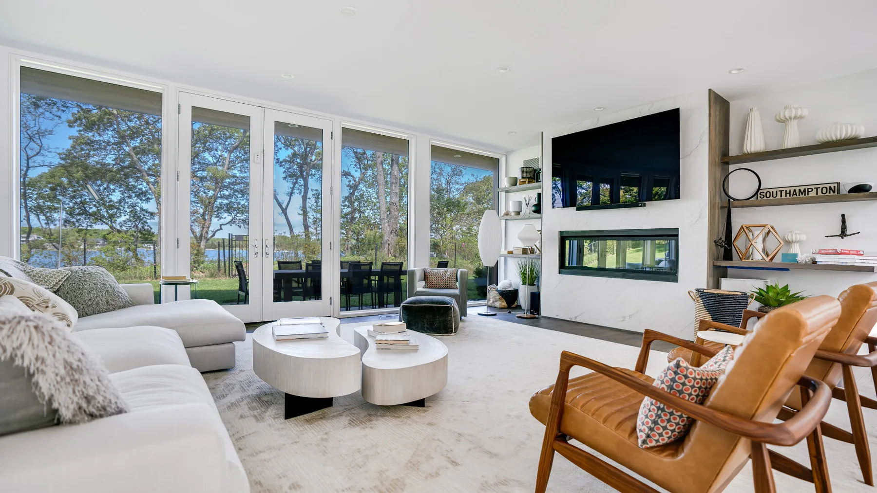 A bright living room with large windows, a white sectional, and wooden seating.