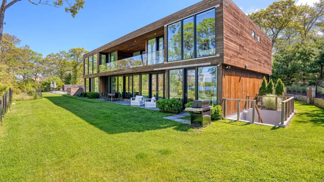 A modern two-story house with large windows overlooks a broad green lawn.