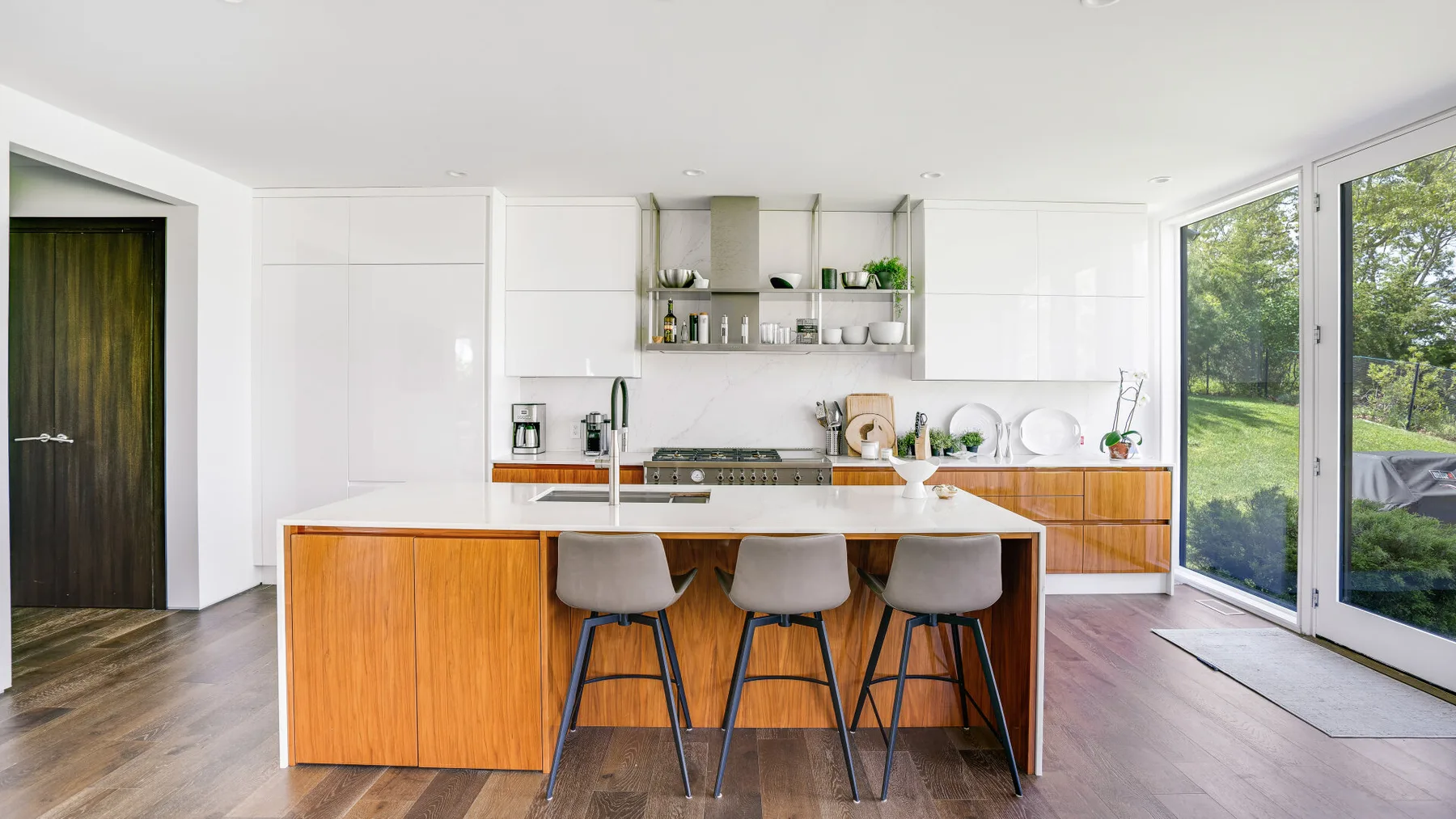 A bright kitchen with a wood-fronted island and large glass doors opening onto greenery.