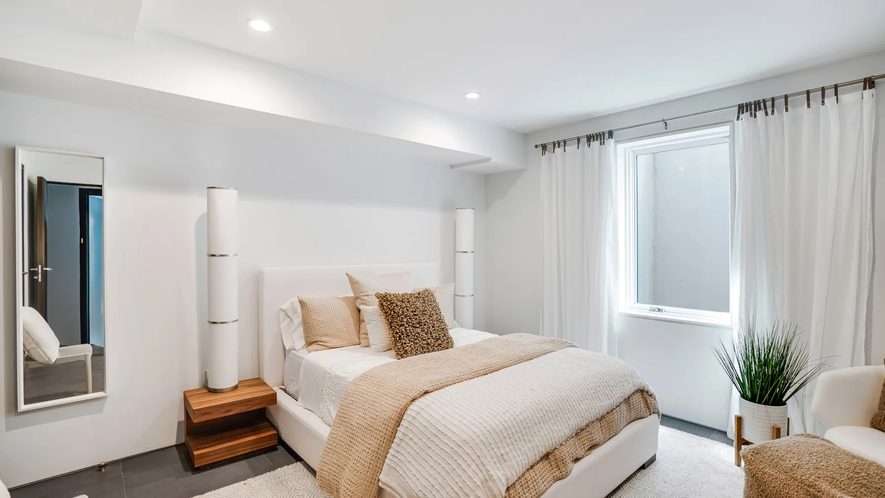 A bright bedroom with a neatly made bed beside a curtained window.