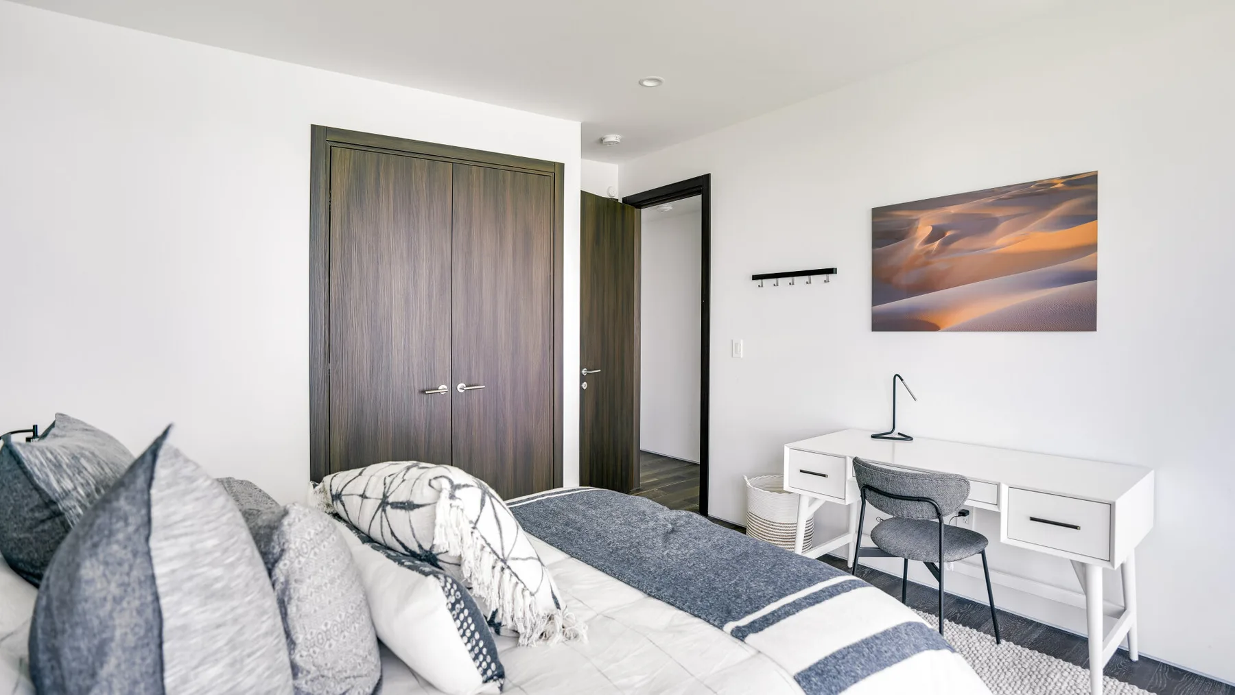 A bedroom with a bed, a desk, and a landscape picture on the wall.