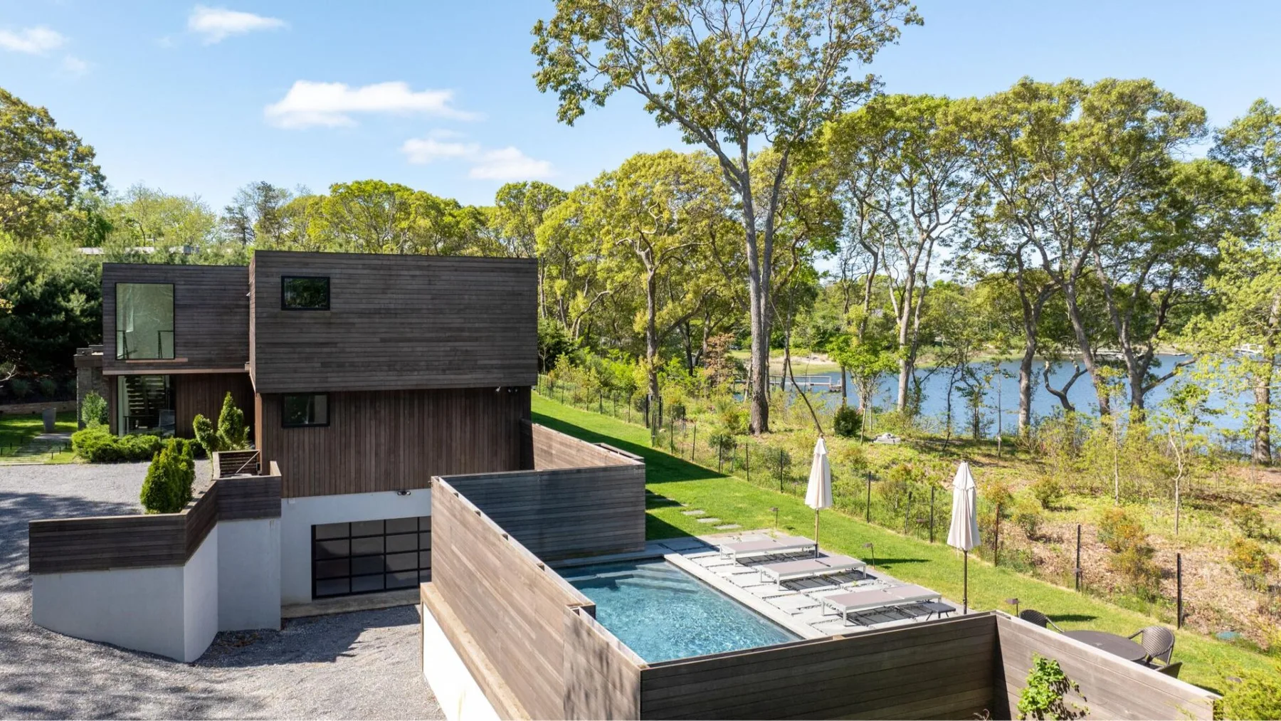 A modern house overlooks an outdoor pool and a wooded lakeside.