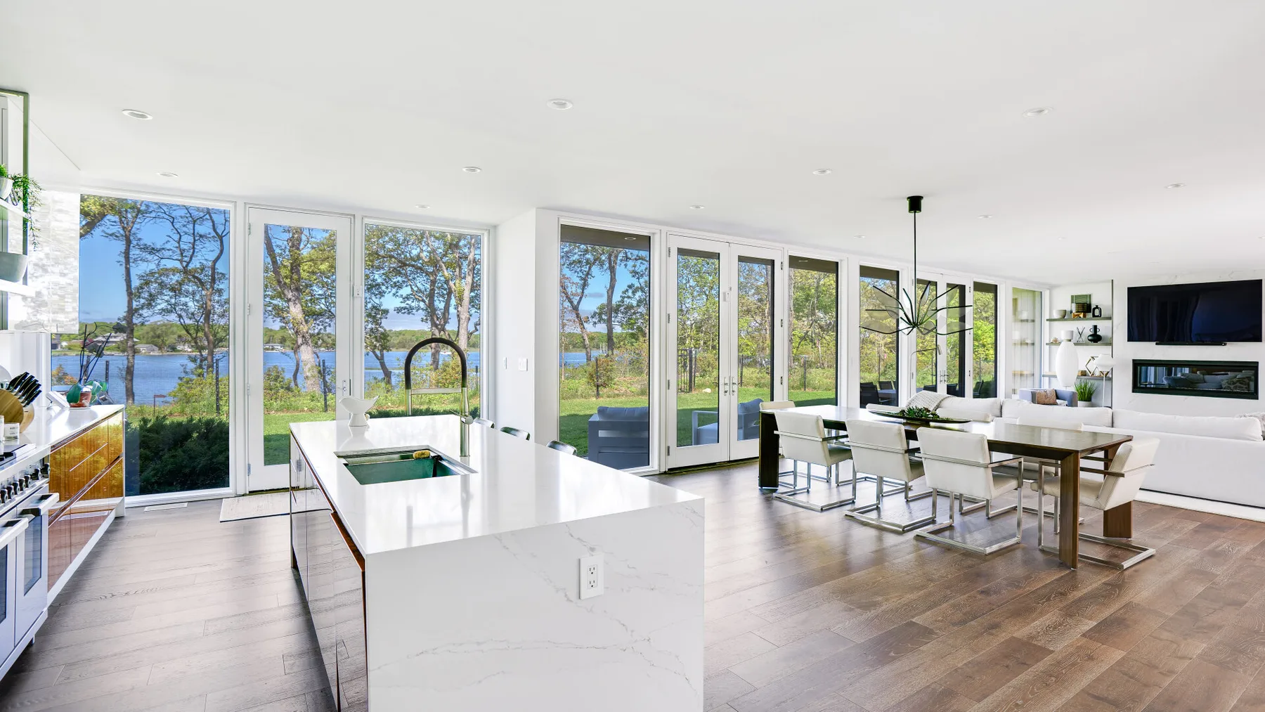 A bright open-plan kitchen and dining area with large windows overlooking greenery and water.