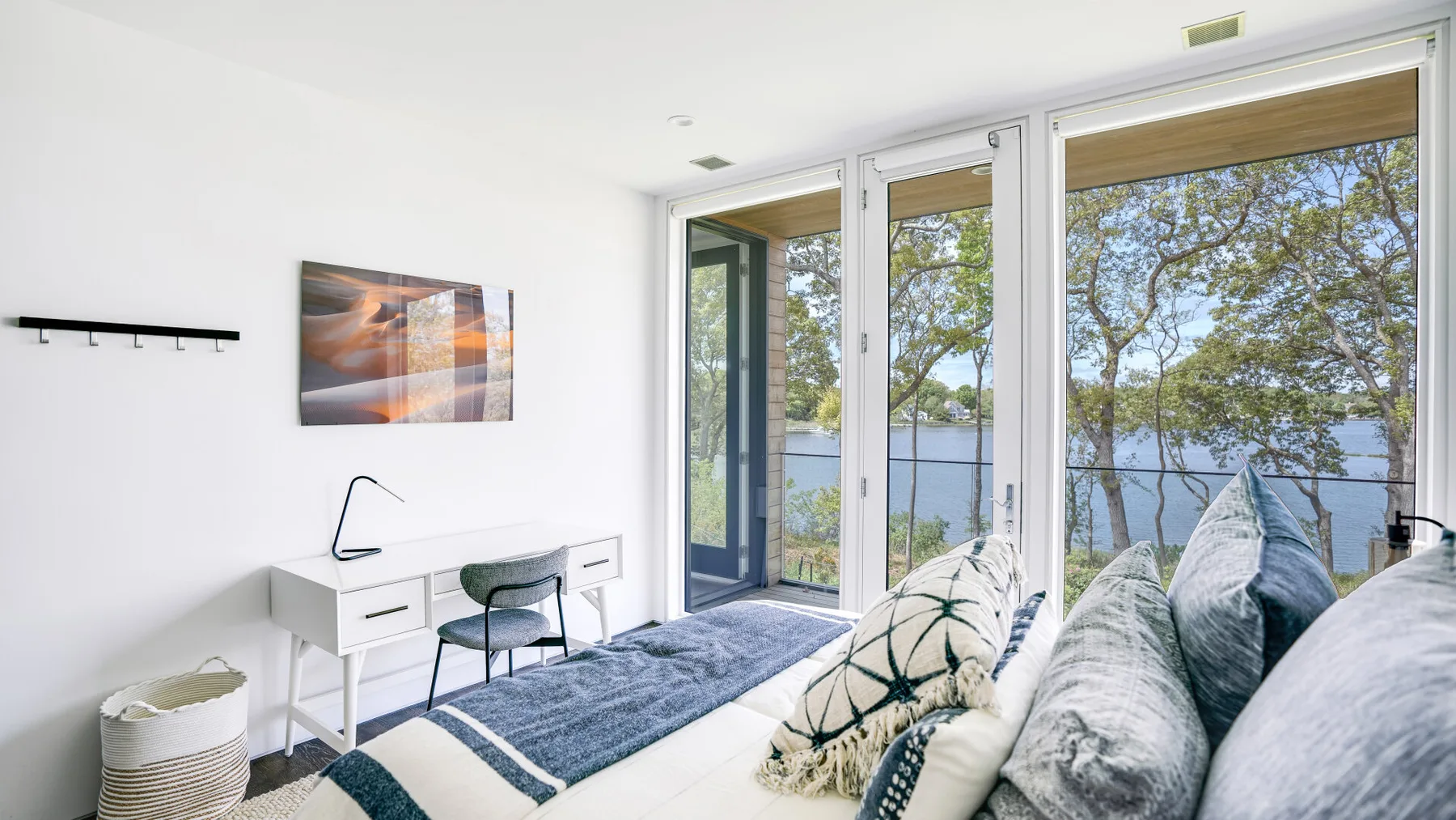 A bright living room with seating beside large windows overlooking trees and water.