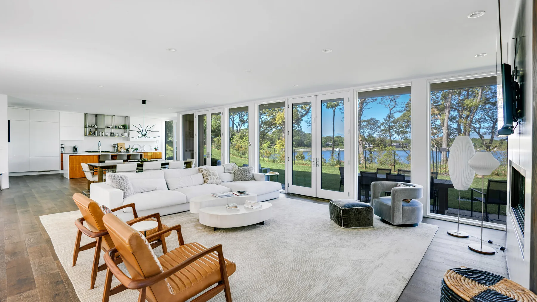 A bright living room with seating arranged beside large windows overlooking trees and water.