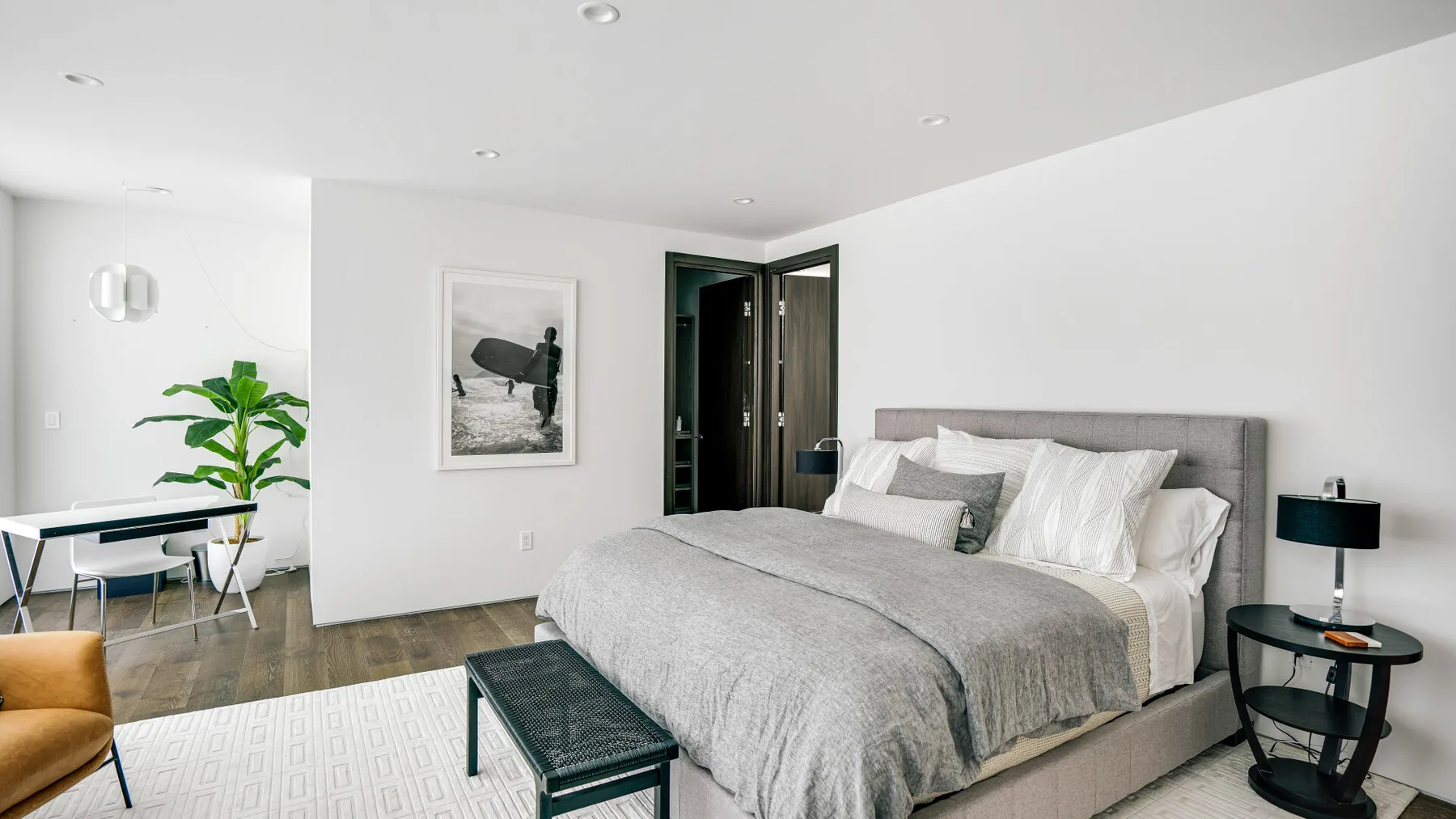 A bright bedroom features a large bed with gray bedding and a bedside table.