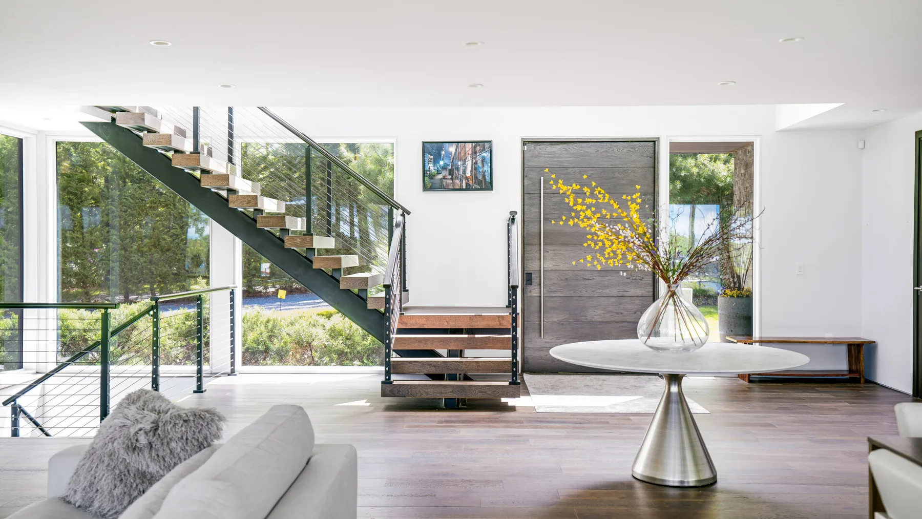 A bright open living area with a staircase, seating, and a round table.