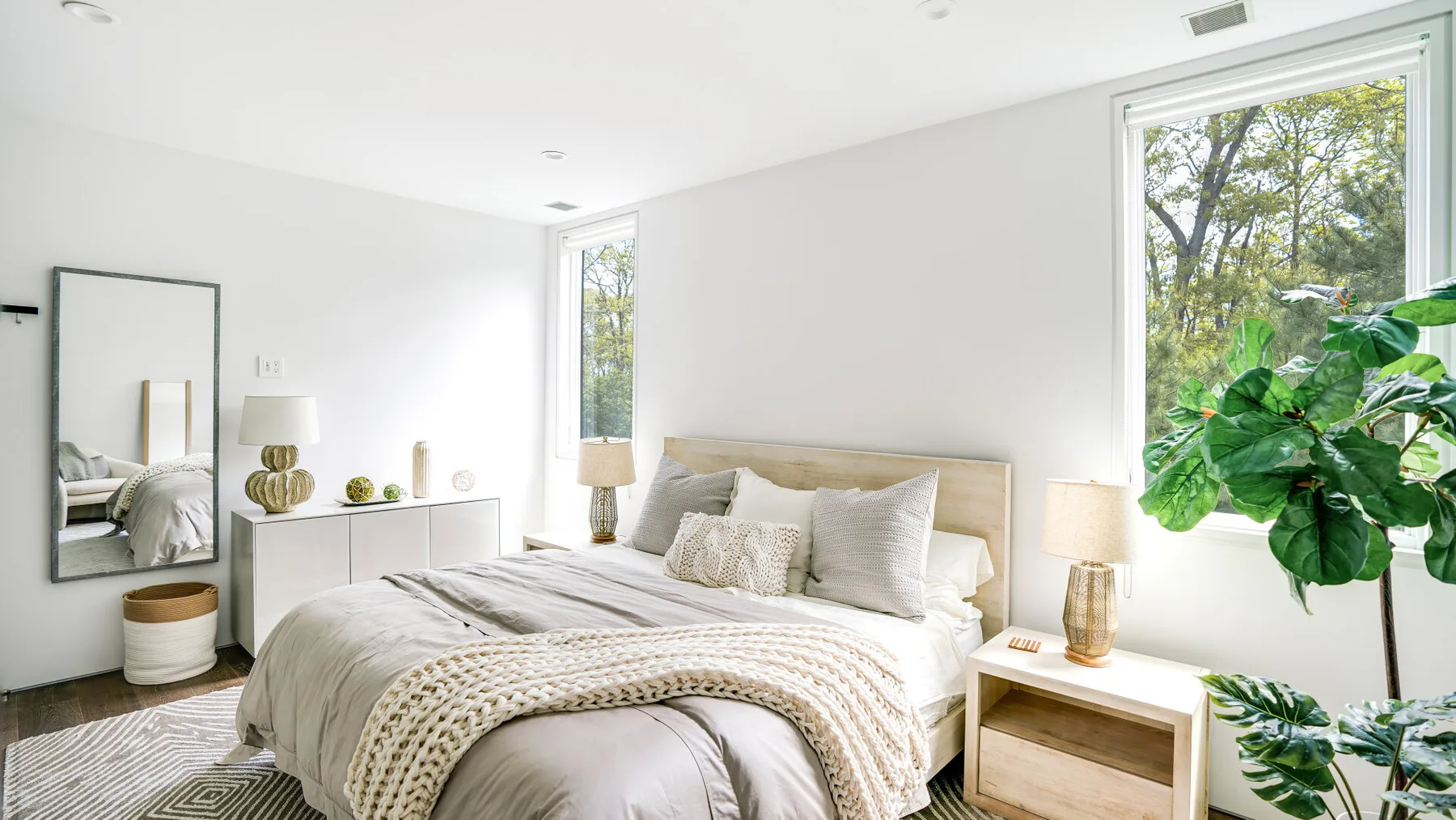 A bright bedroom with a bed, bedside tables, and large windows.