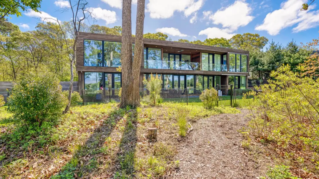 A modern glass-fronted building sits among trees beside a gravel path.