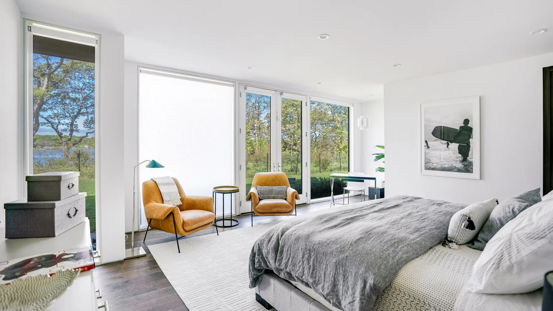 A bright bedroom with a large bed and mustard-colored seating beside tall windows.