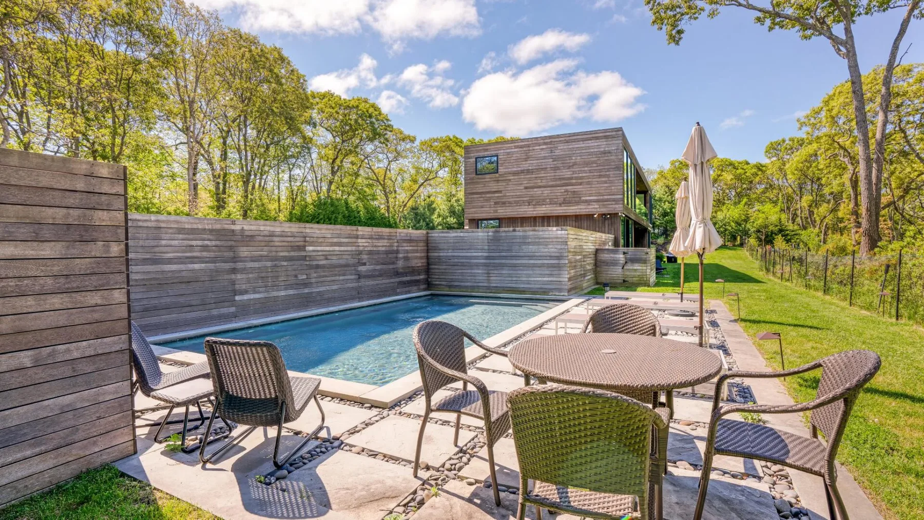 Un patio exterior con piscina, mesa y sillas junto a un edificio de madera.
