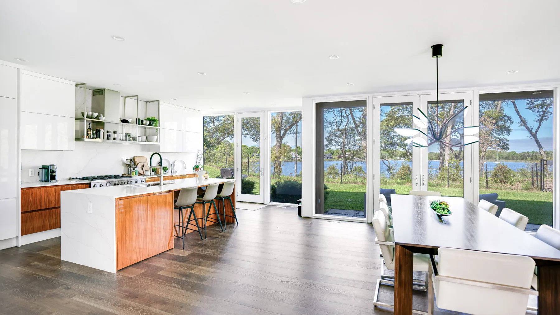 A bright open-plan kitchen and dining area overlooks a lawn and water.