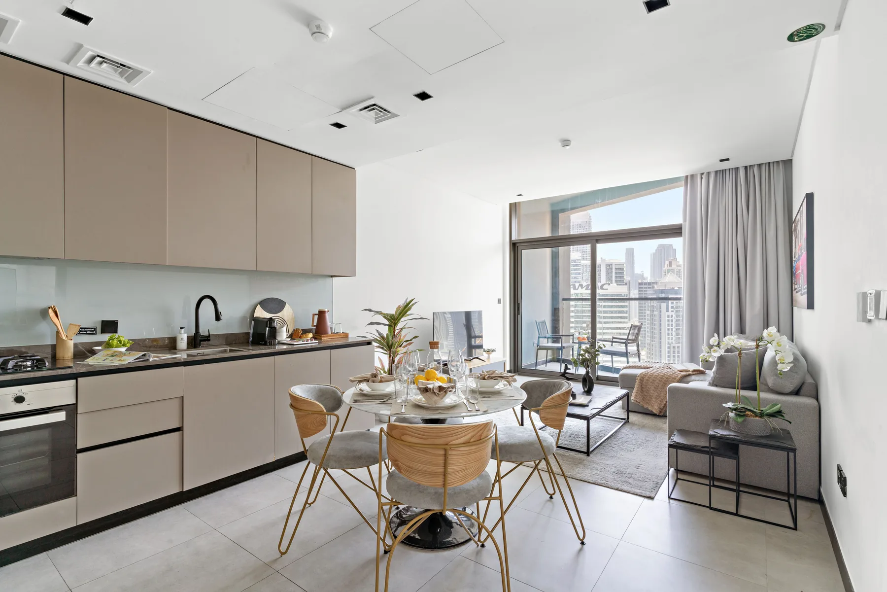 A bright open-plan living and dining area with a table beside large windows.