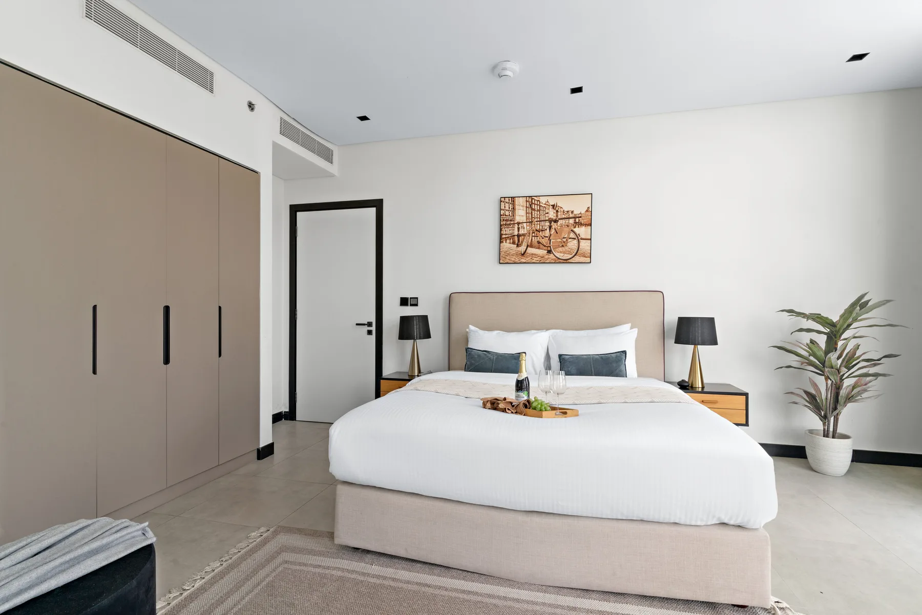 Bedroom with a neatly made bed, bedside tables, and a potted plant.