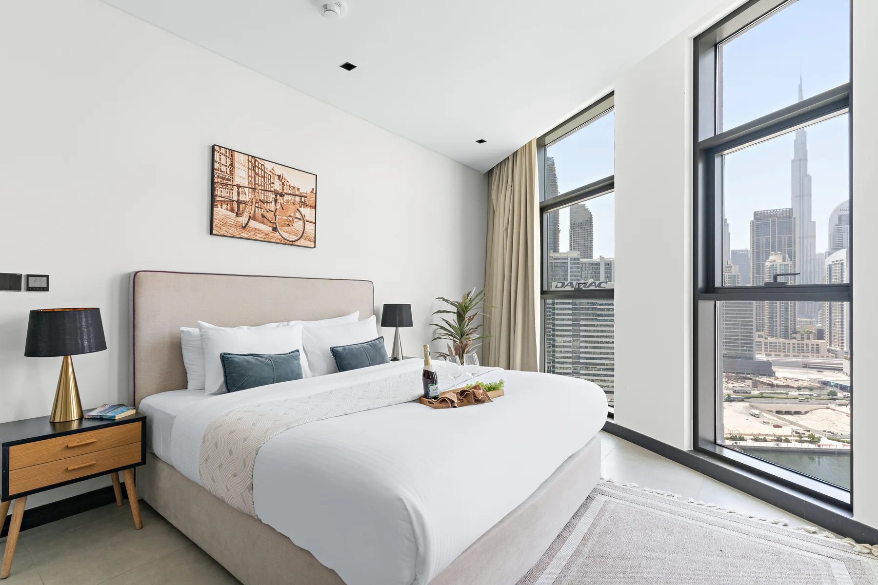 A bright bedroom with a neatly made bed beside floor-to-ceiling windows.