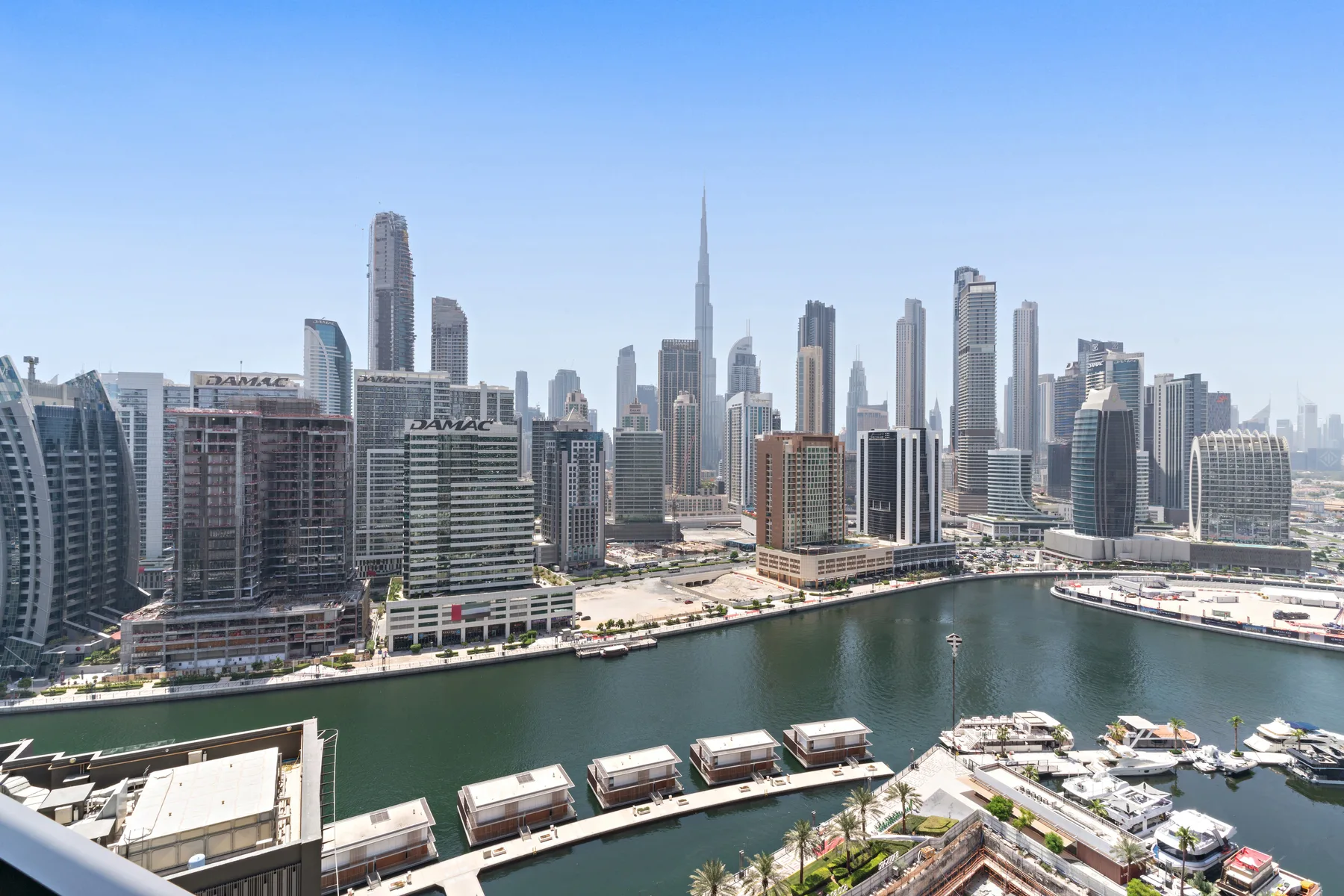 A city skyline rises behind a marina and waterfront promenade.