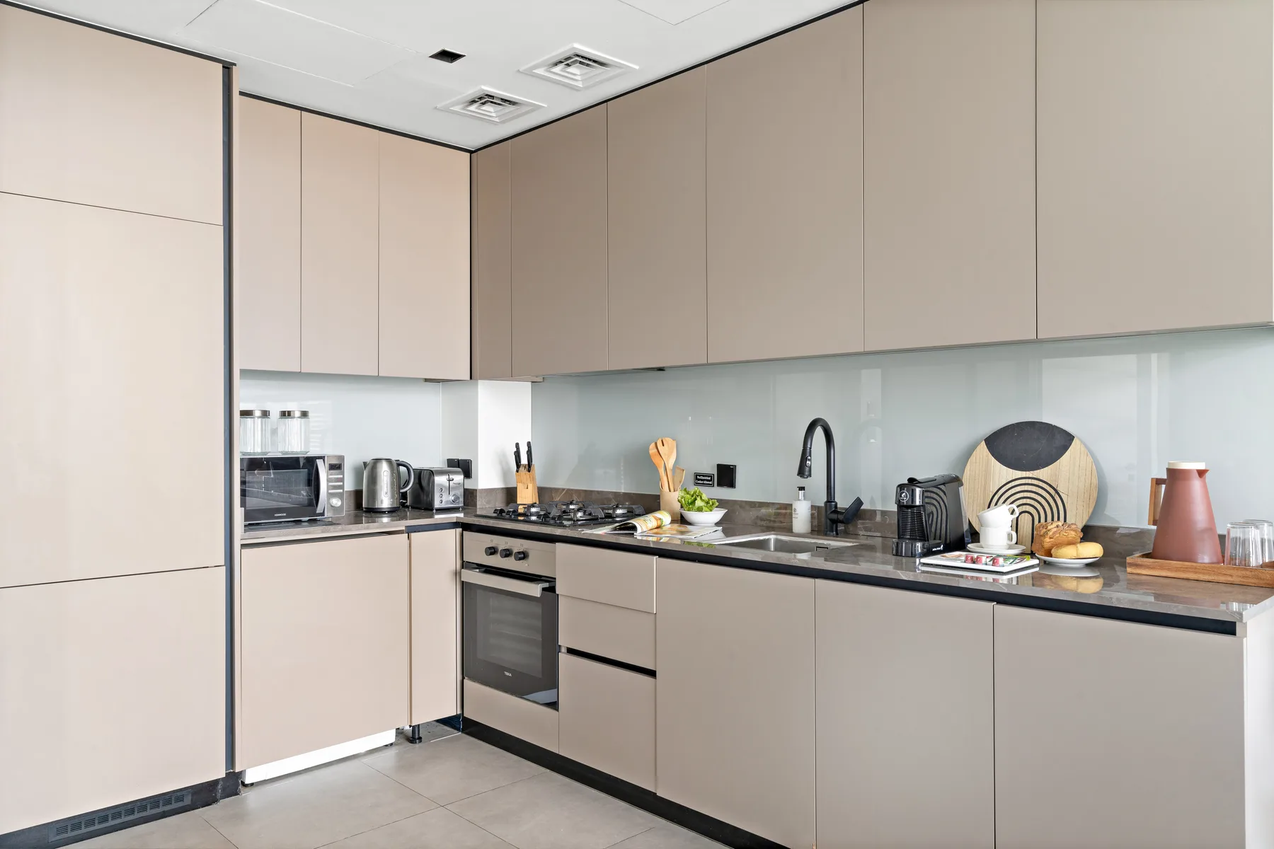 A modern kitchen with pale cabinets, dark countertops, and stainless steel appliances.
