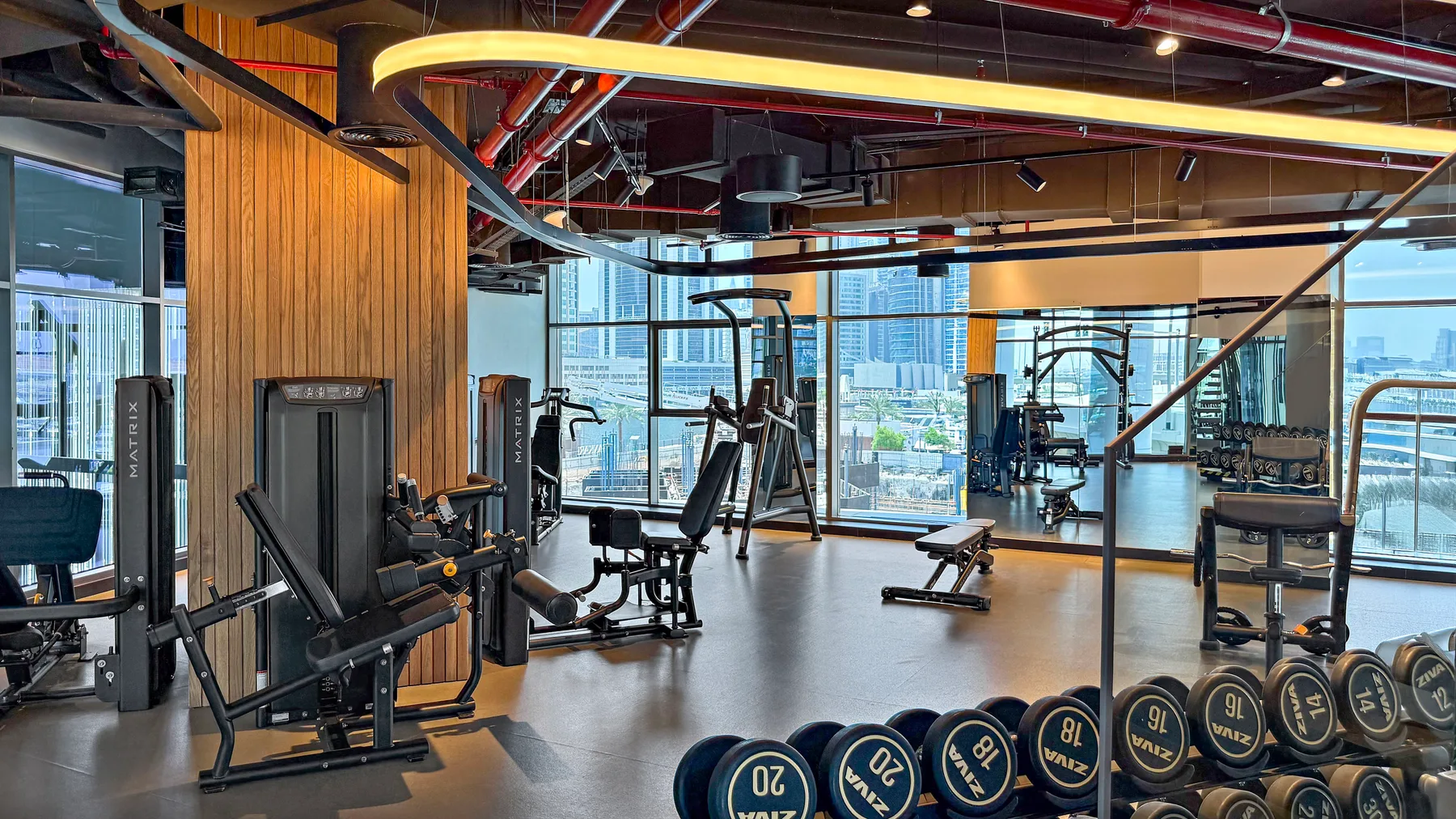 A fitness room with weight machines and dumbbells beside large windows.