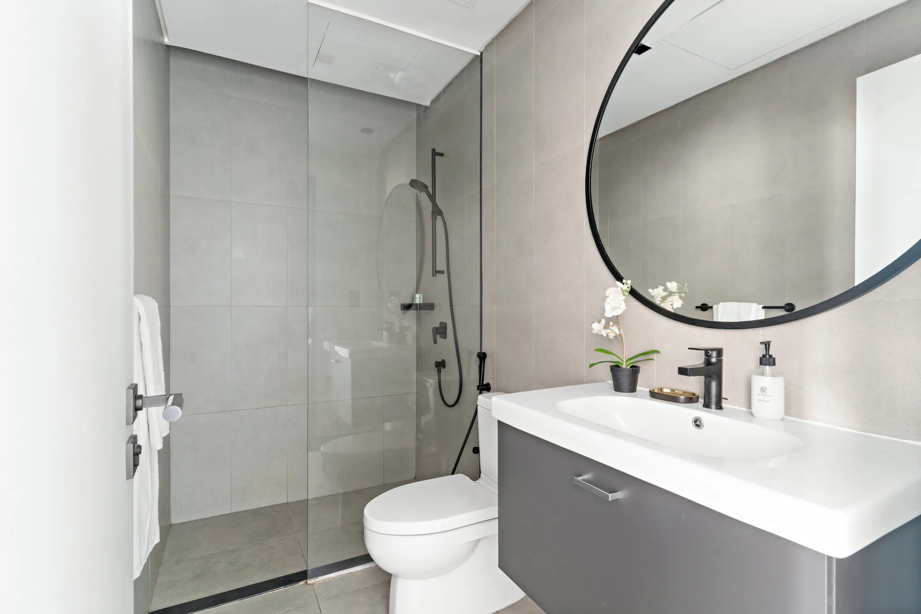 A modern bathroom with a glass shower, toilet, and wide sink vanity.