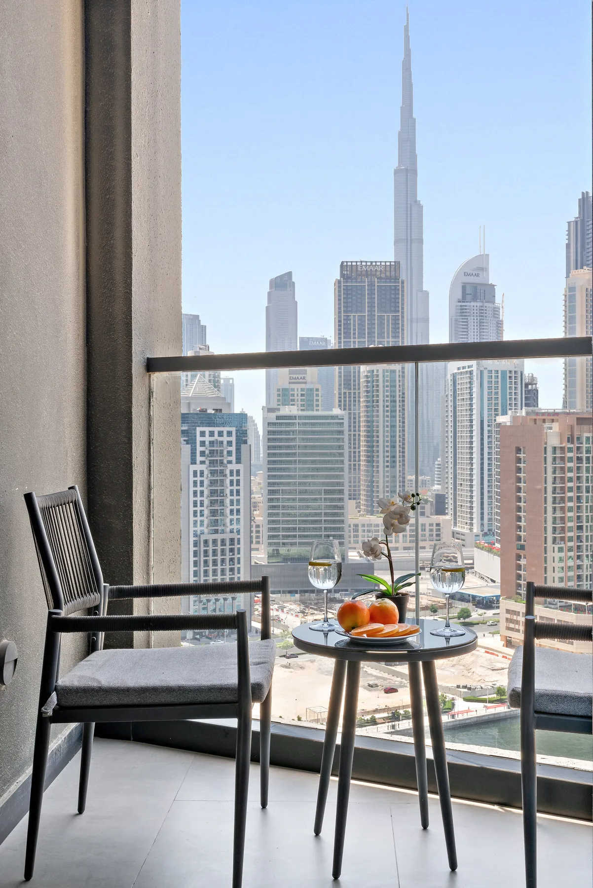 A balcony seating area overlooks a city skyline, with a small table beside the chairs.