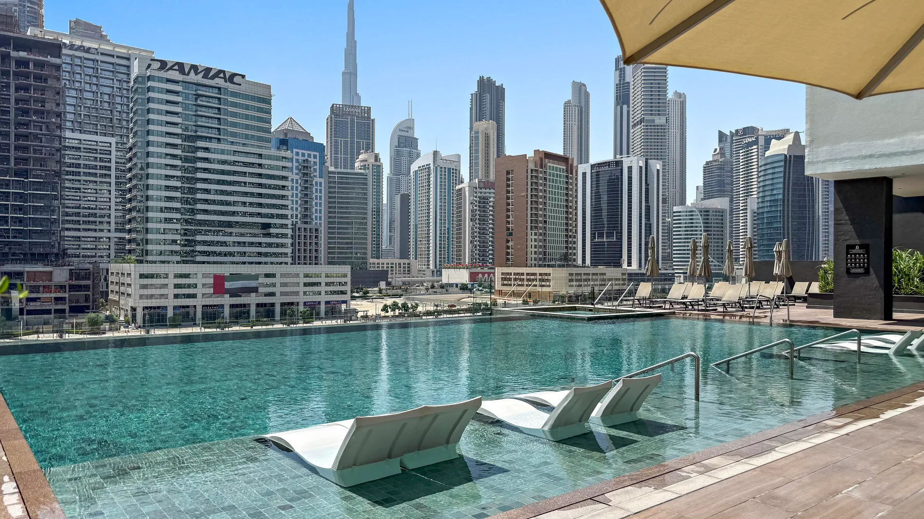 A rooftop swimming pool overlooks a dense skyline of modern high-rise buildings.