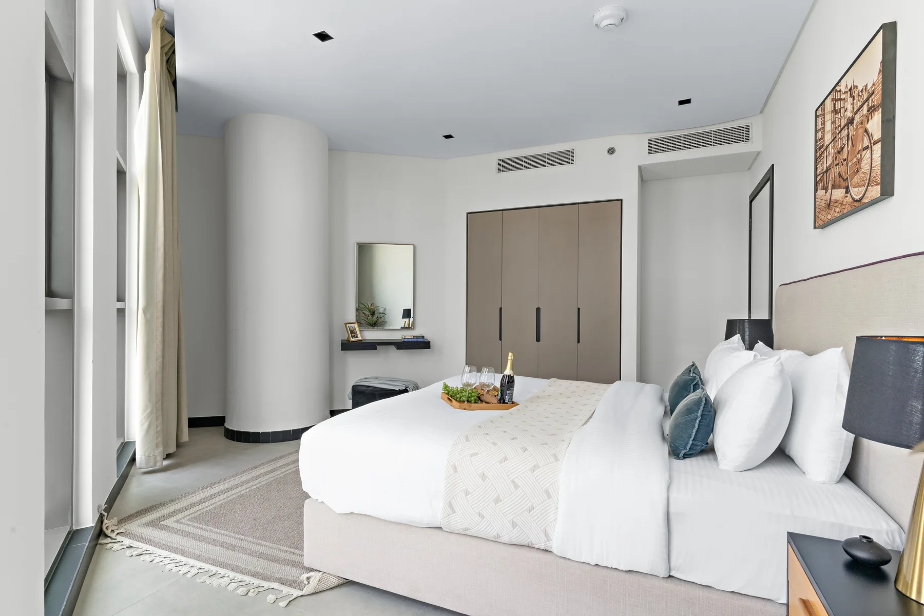 A bright bedroom with a neatly made bed and framed artwork on the wall.