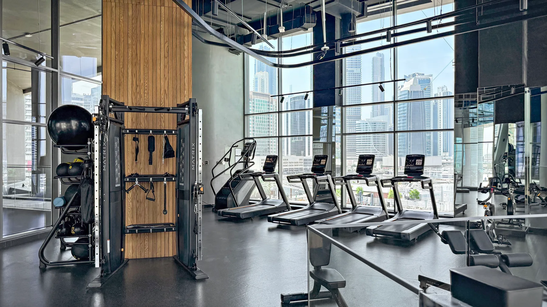 A gym with treadmills, exercise equipment, and large windows overlooking the city.