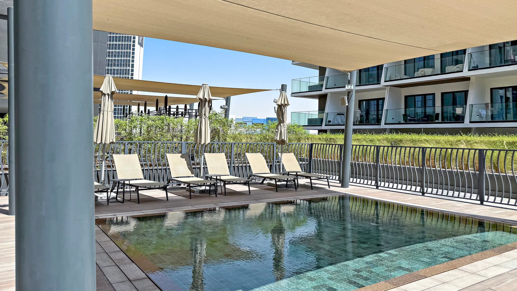 An outdoor pool beneath a shaded terrace, with lounge seating along the edge.