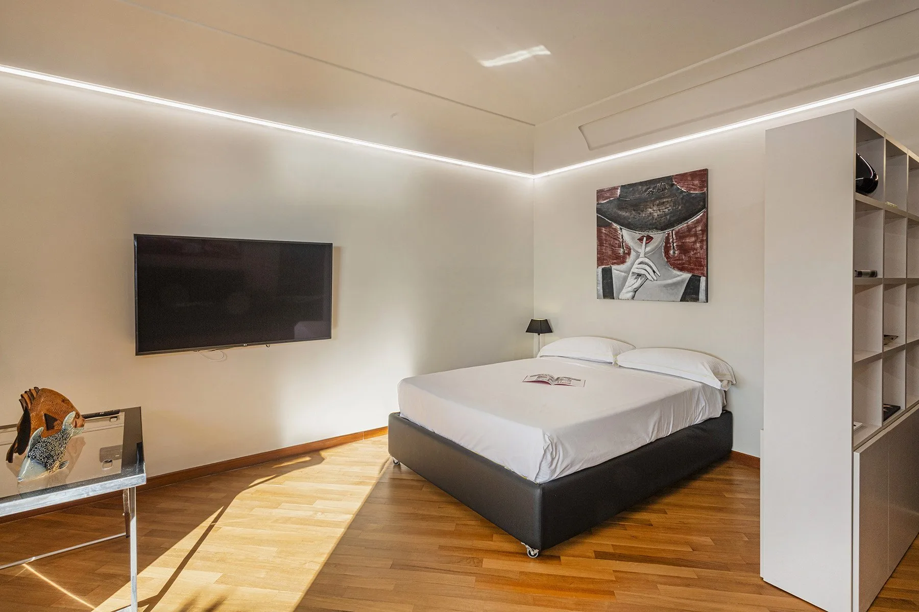 A bedroom with a bed, wall-mounted television, and wooden flooring.