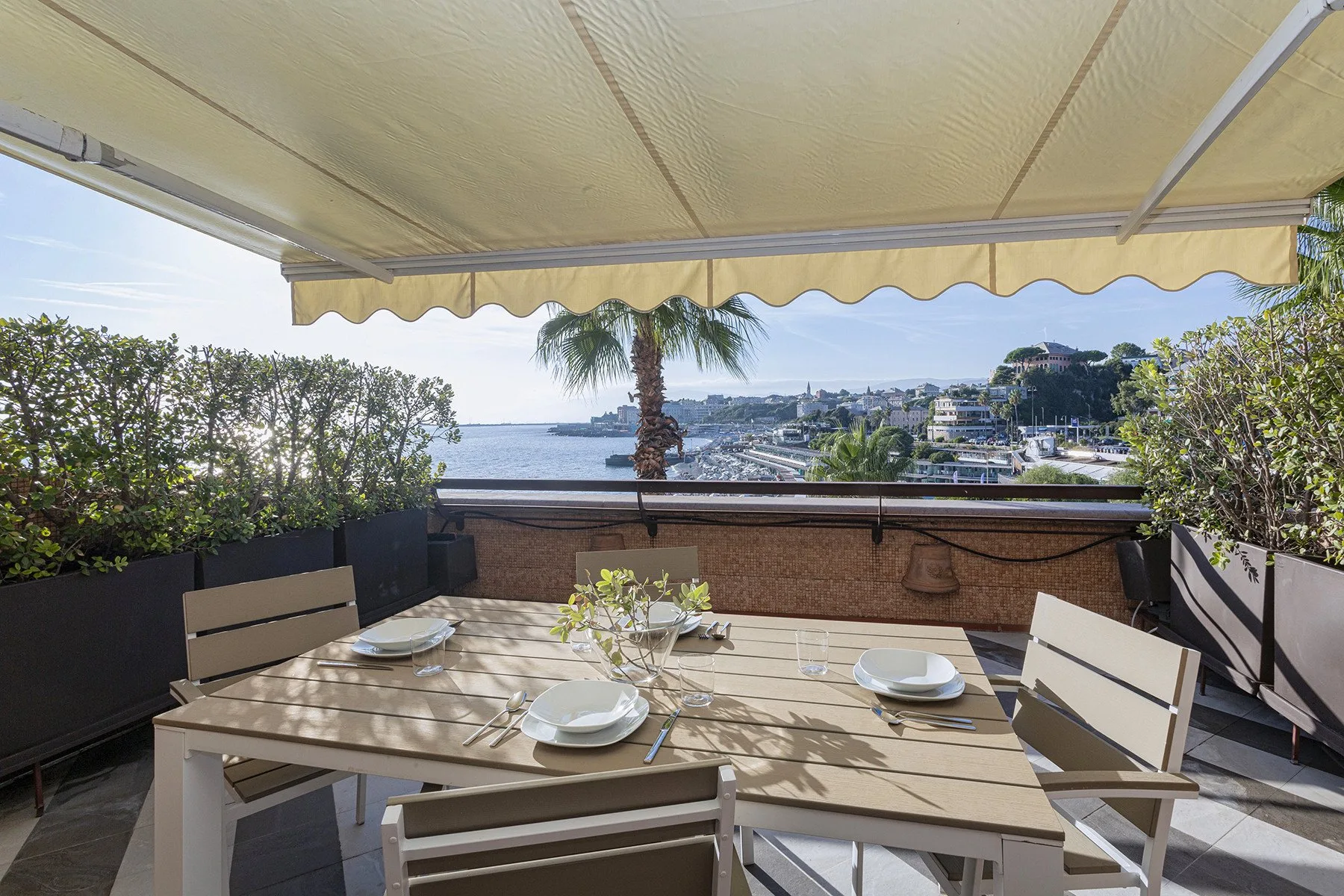 Una zona de comedor exterior a la sombra, con la mesa puesta y vistas al agua.