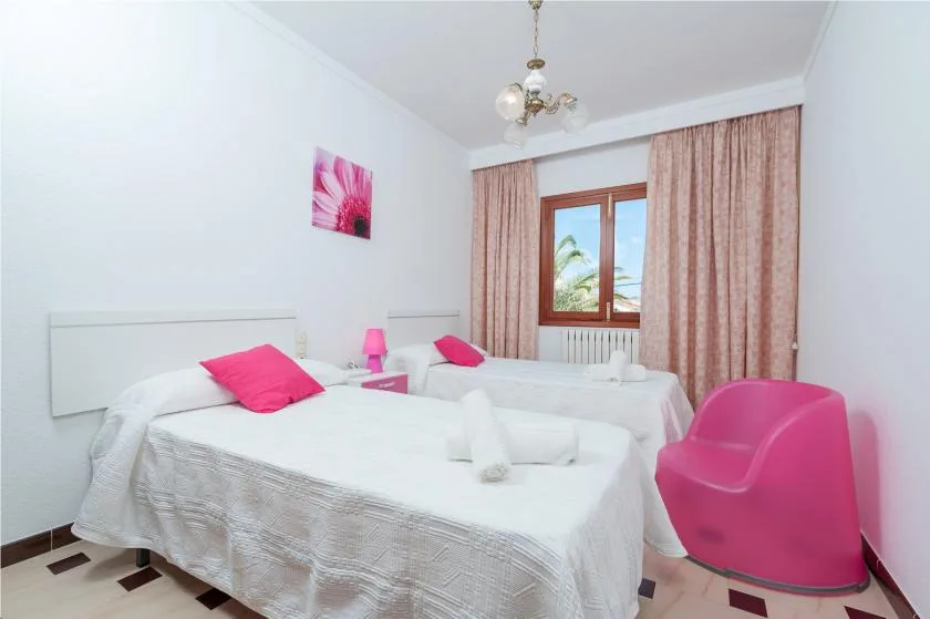 A bright bedroom with white bedding, pink seating, and a curtained window.