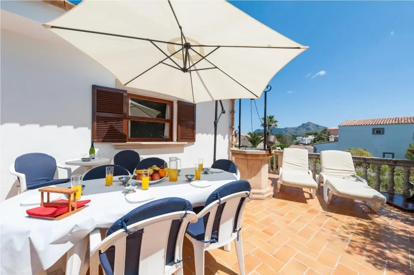 Una terraza soleada tiene una mesa de comedor al aire libre bajo una gran sombrilla.