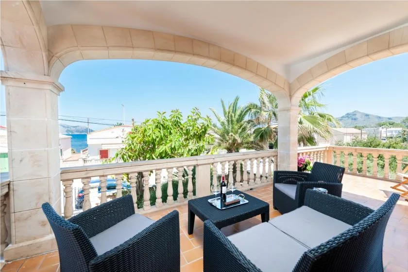 A covered terrace with cushioned seating and a low table overlooks greenery.