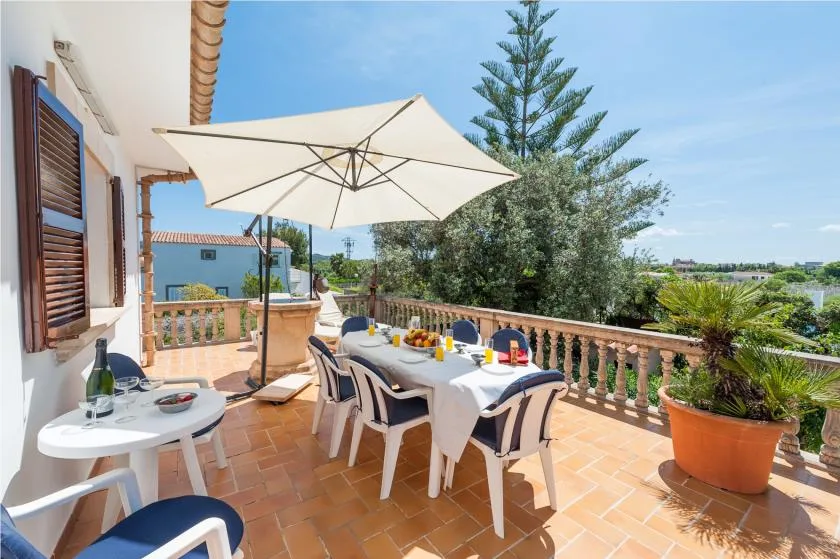 An outdoor dining terrace with a table, chairs, and a large shade umbrella.